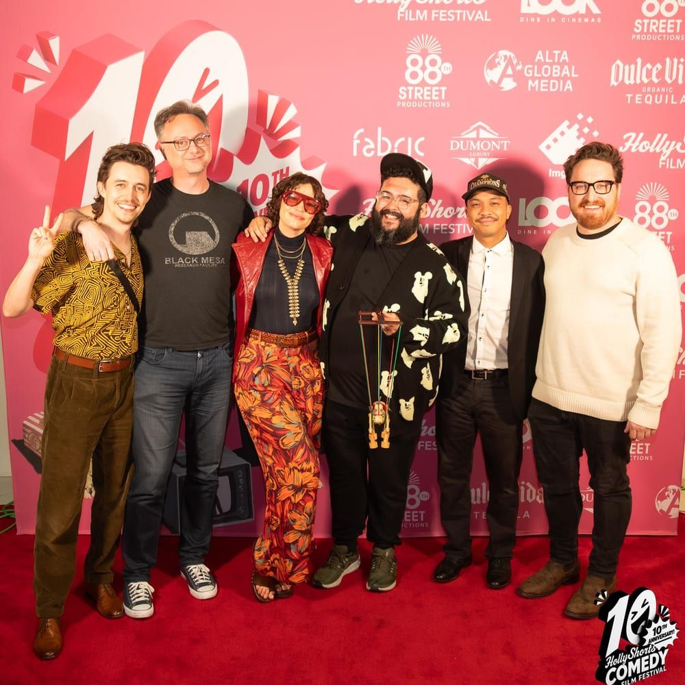 Six members of the cast and crew on the red carpet at the HollyShorts Comedy Film Festival, one holding the wooden horse puppet from the poster